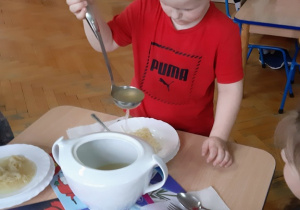 Filipek nalewa zupę z wazy na talerz.